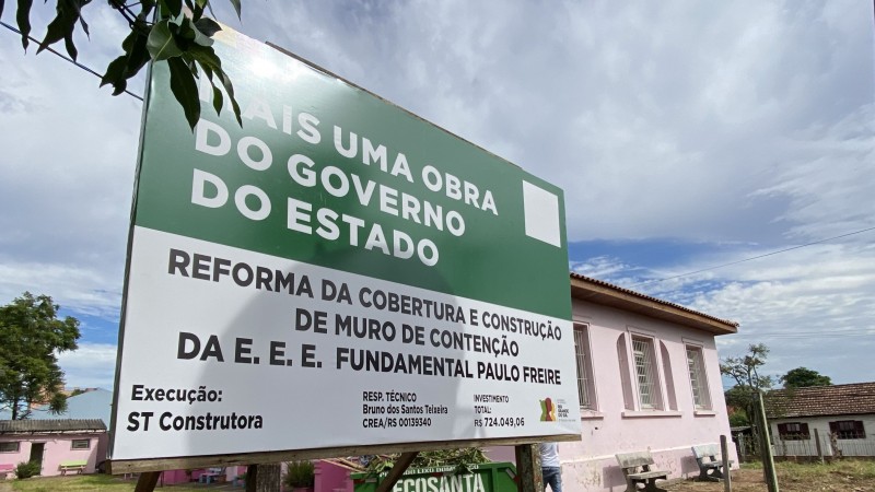 Fachada da Escola Paulo Freire, em Santa Maria, com uma placa de obras do governo do Estado em close.