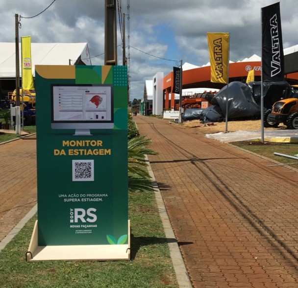 Totens com QR Code para acesso ao site foram instalados no parque da Expodireto Cotrijal, em Não-Me-Toque. Na imagem, um totem verde com QR Code e reprodução de imagem do site aparece no canteiro central de uma via interna do parque.
