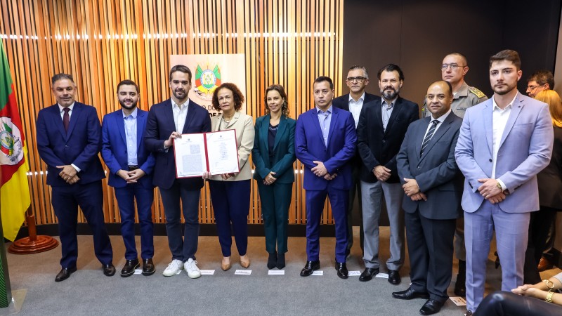 O governador Eduardo Leite, ao lado da presidente do TJ, Iris Helena, segura uma mostrando o termo de cooperação assinado. Ao deles, também posam para foto o vice-governador, Gabriel Souza, o procurador-geral de Justiça, Marcelo Dornelles, os secretários da SSP, Sandro Caron, e da SSPS, Luiz Henrique Viana, o diretor executivo do RS Seguro, Alexandre Padilha, o chefe da PC, Fernando Sodré, o comandante da BM, Cel. Feoli, e o chefe da Susepe, Mateus Schwartz.