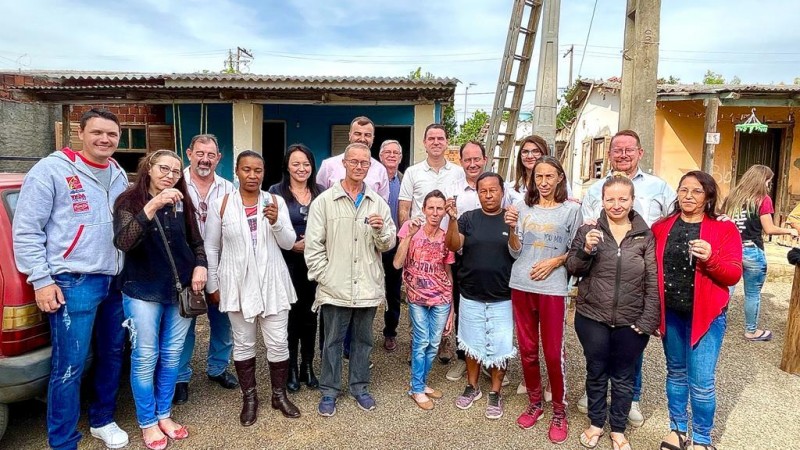 Grande grupo de pessoas posa para foto diante de uma casa em uma de um bairro de Venâncio Aires. Várias belas seguram nas mãos chaves das unidades sanitárias entregues pelo Programa Nenhuma Casa Sem Banheiro. Entre as pessoas no grupo, bem ao centro, está o secretário de Habitação e Regularização Fundiária, Fabrício Perucchin.