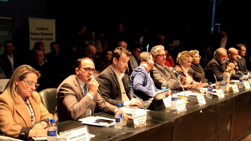 Da esquerda para a direita, sentados atrás de uma grande bancada, estão Danielle Calazans, Bruno Jatene e Artur Lemos, na audiência pública realizada na Assembleia Legislativa para tratar da reformulação do IPE Saúde. Há outras pessoas nas foto, sentadas na continuação da bancada.