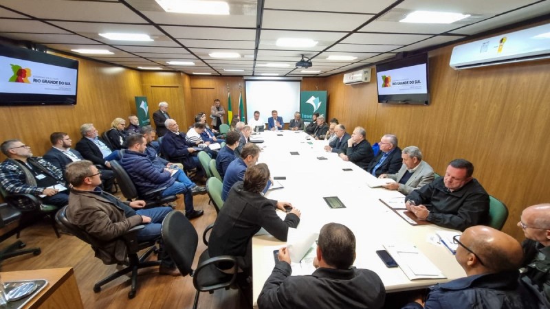 Várias pessoas se encontram sentadas à mesa, numa reunião