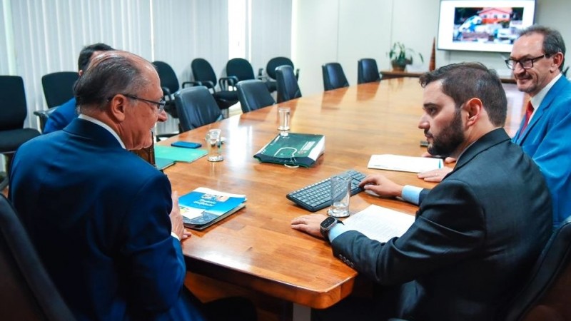 Alckmin de costas sentado na cabeceira de uma mesa grande do lado esquerdo da foto. Gabriel de lado, à direita da imagem. Os dois conversam e há mais duas pessoas na reunião: uma ao lado de Gabriel e outra de frente para ele, do outro lado da mesa.