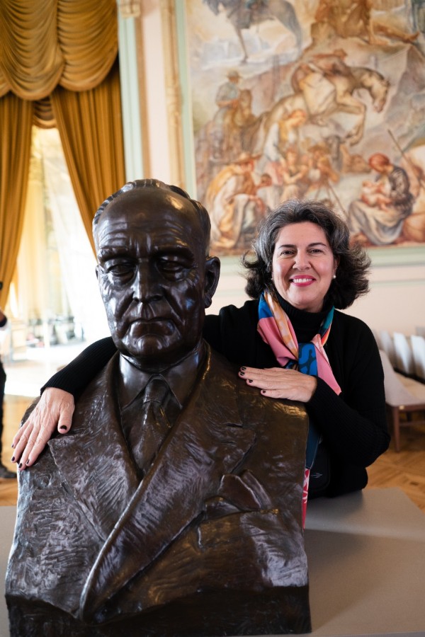 Antonella se posiciona logo atrás do busto de Getúlio Vargas, o qual toca com as mãos