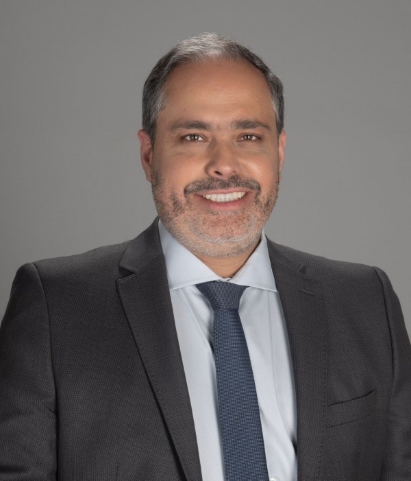 Retrato de Gustavo Paim. É um homem branco, com cabelo curto, grisalho e barba grisalha. Olhos castanhos. Na foto, está sorrindo. Veste blazer em cinza escuro, camisa azul clara e gravata azul marinho com listras finas.