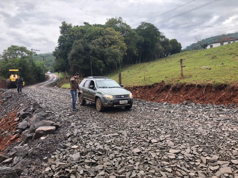 Um carro atravessa o acesso, passando por um homem parado. Ao fundo, um trator amarelo