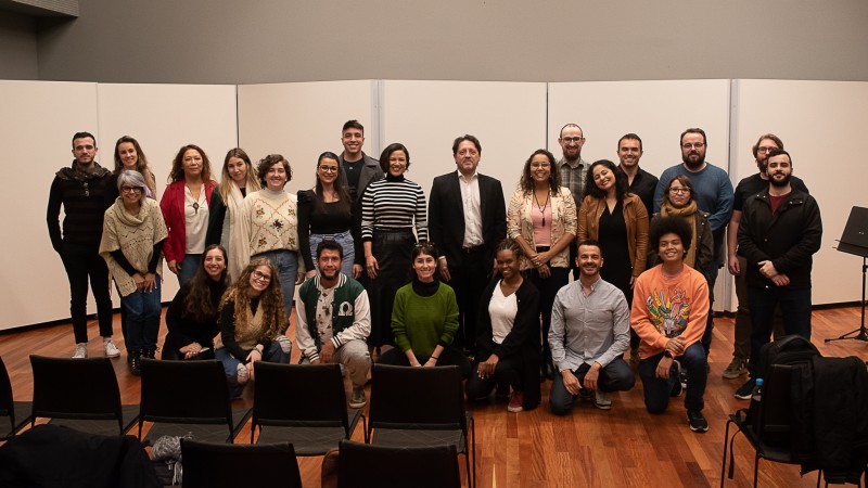 24 integrantes do projeto, com o maestro ao meio, posam numa sala da Ospa. Alguns estão de pé; outros, agachados à frente