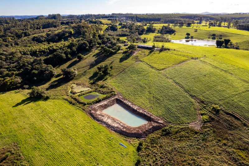 Tomada área de um açude, rodeado pelo campo verde e pela mata