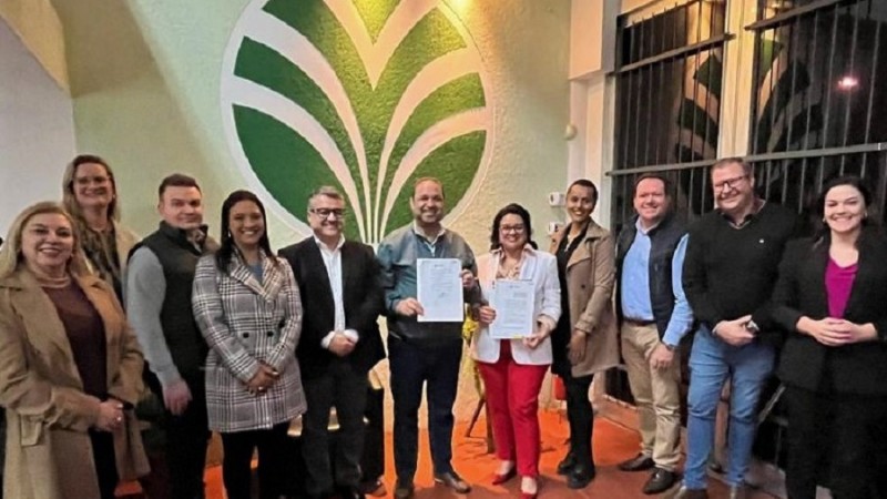 Onze pessoas diante de um painel que representa uma árvore na sede da Fetag/RS. No centro da imagem está a secretária de Meio Ambiente e Infraestrutura segurando o documento assinado.