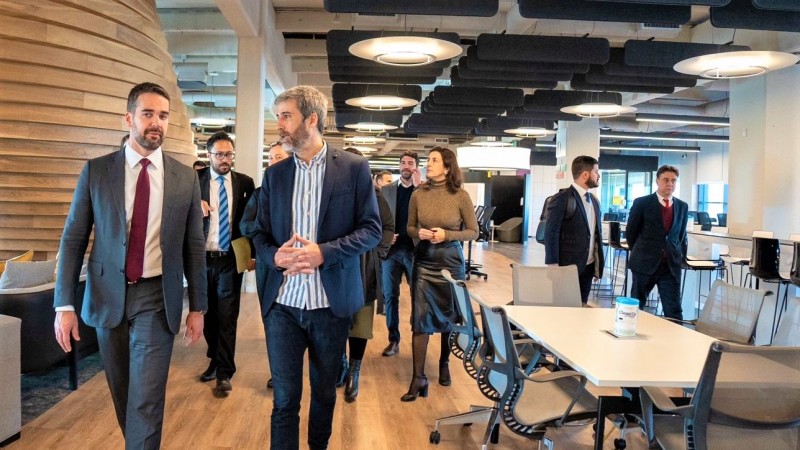 Leite caminhando ao lado de um representante do Mercado Livre, seguidos por diversas pessoas. O ambiente é amplo com mobiliário próprio de escritório.