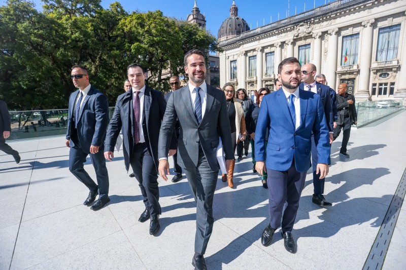 Em ambiente aberto, governador Eduardo Leite caminha ao lado do vice-governador Gabriel Souza em direção à Assembleia Legislativa. Ao fundo, aparece o Palácio Piratini e o domo da Catedral.