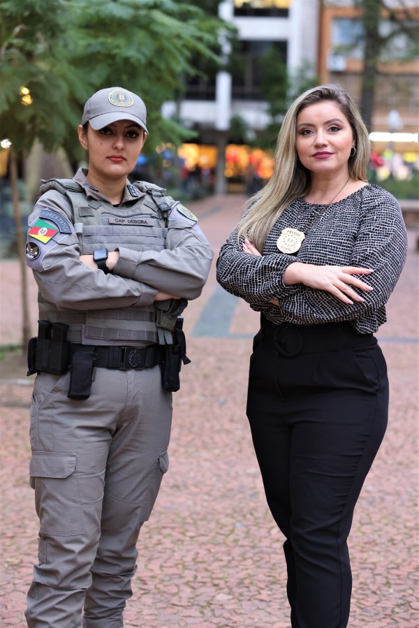 Foto posada em que a delegada Cristiane Ramos (à direita), diretora da Divisão de Proteção à Mulher da Polícia Civil, e a capitã Débora Rocha (à esquerda, comandante da Patrulha Maria da Penha no 21º Batalhão de Polícia Militar (BPM), estão em pé e de braços cruzados, tendo a Praça da Alfândega desfocada ao fundo.