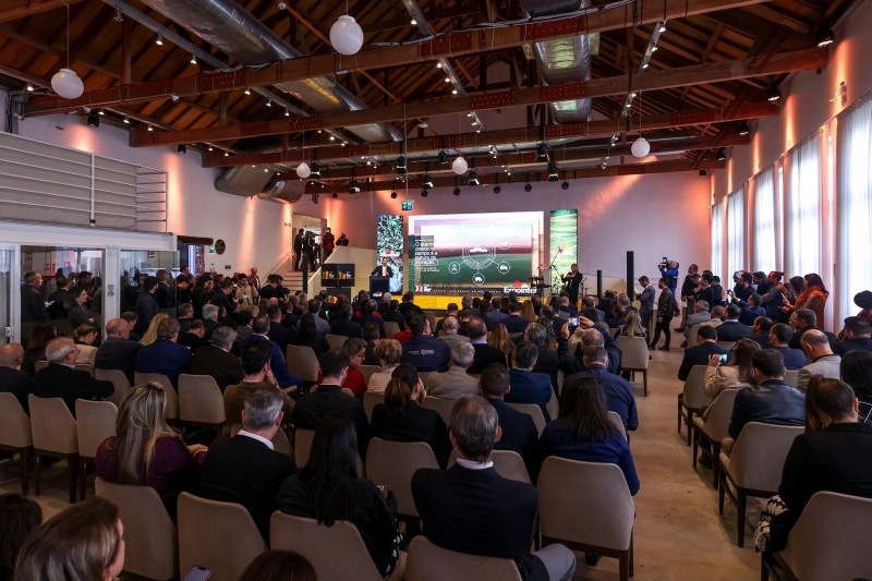 Ambiente fechado. Imagem aberta mostra o espaço do lançamento da Expointer 2023, com diversas cadeiras ocupadas pela plateia. No palco frontal, há um painel digital.