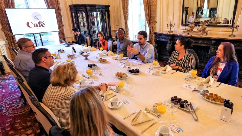 Leite no centro da imagem sentado à mesa da sala de banquetes do Palácio Piratini falando com os participantes do Café com Gov que estão sentados à sua direita, à sua esquerda e à sua frente. Na imagem a mesa está posicionada diagonalmente do canto esquerdo superior para o canto esquerdo inferior.