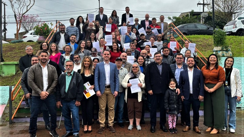 Foto posada em uma escadaria com inúmeras pessoas mostrando o termo de legitimação fundiária que receberam do governo do Estado.