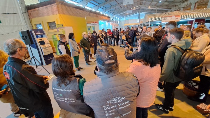 Secretária Ronaldo Santini, com um chapéu de palha, discursa em microfone para um grupo de produtores reunidos na praça de alimentação do Pavilhão da Agricultura Familiar, na Expointer.