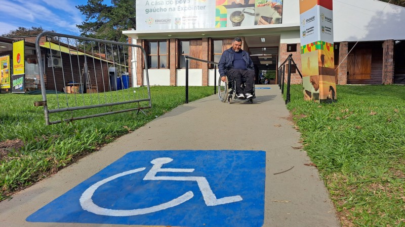 Marco Antônio Lang, cadeirante, aparece em uma pista com asfaltamento e barras laterais construída no Parque de Exposições Assis Brasil para facilitar a mobilidade de pessoas com deficiência durante a 46ª Expointer. Em primeiro plano, no piso da pista, aparece o símbolo de reserva de estacionamento para cadeirantes. Foto Fernando Dias/Seapi