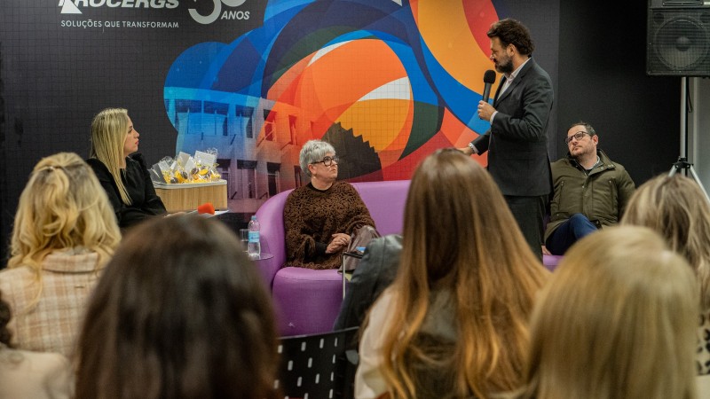 Antônio Padilha ao microfone e em pé falando para a plateia durante a entrega do selo. Ele olha para uma mulher sentada em um sofá. Na imagem podem ser vistas cabeças de outras mulheres sentadas e de costas participando da solenidade.