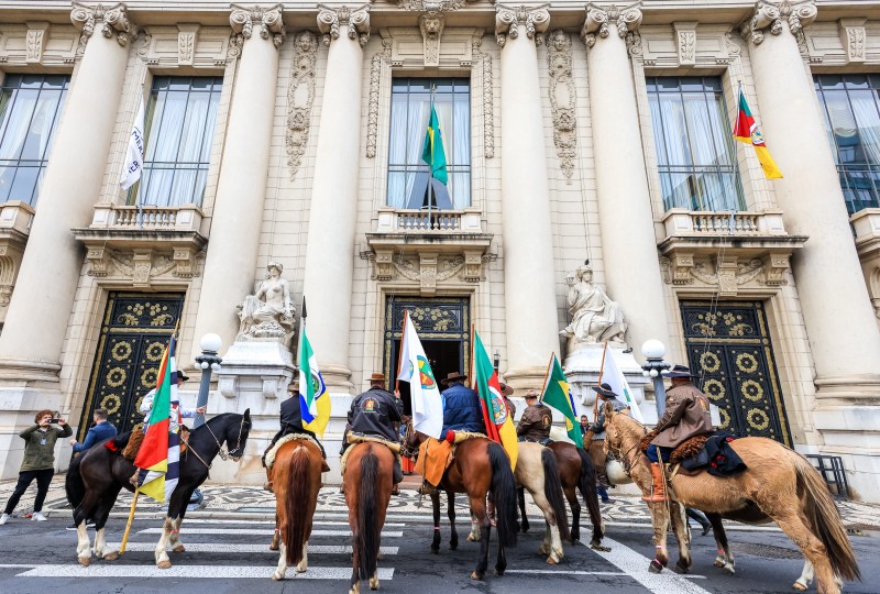 Cavalarianos que trouxeram a Chama Crioula perfilados diante do Palácio Piratini. Eles são vistos de costas com o Palácio ao fundo.