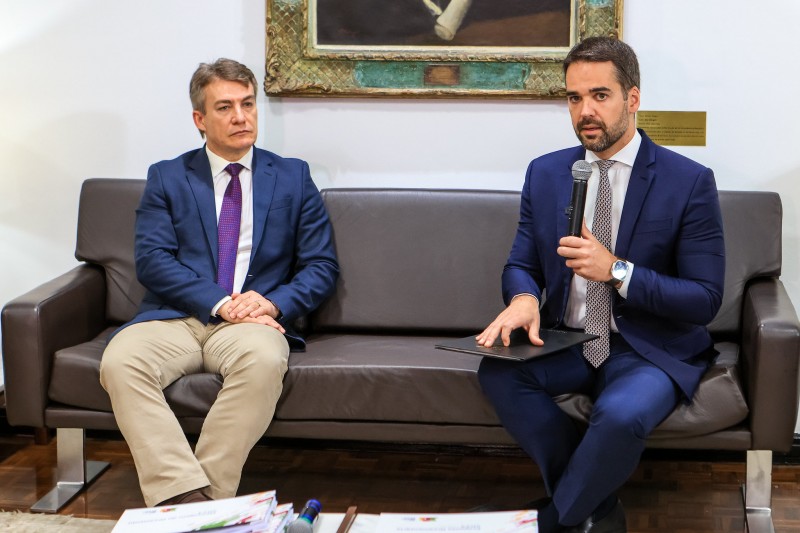 Leite falando, sentado em um sofá, ao lado do presidente da Assembleia, durante o ato de entrega da PLOA 2024