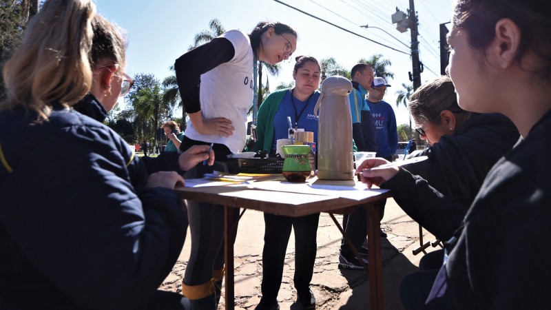 Pessoas das equipes em volta de uma mesa em local aberto realizando cadastramento de pessoas atingidas pelas enchentes em Roca Sales 2023.