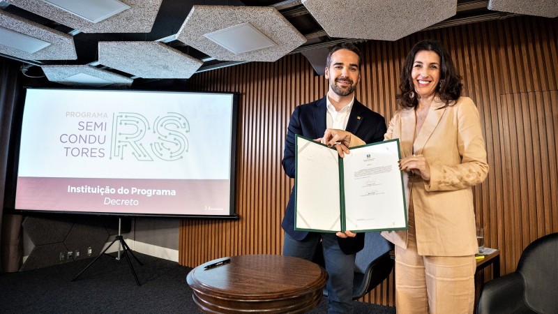 Leite e Simone em pé à direita da imagem seguram o documento que instituiu o programa Semicondutores RS. À esquerda da imagem vê-se uma tela com nome do programa.