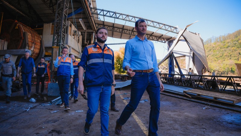 Gabriel Souza visita curtume de Muçum. Ele está no centro da imagem conversando com o dono da empresa e caminhando. Ao fundo podem ser vistas, mais à esquerda, pessoas que acompanham a visita e, à direita, parte das instalações danificadas pela enchente.