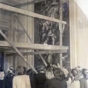 Foto em preto-e-branco mostra várias pessoas, de costas, olhando a pintura de Locatelli na parede no salão, parcialmente coberta por andaime de madeira.