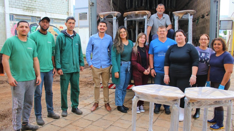 Foto posada, em ambiente aberto, em frente à carroceria de um caminhão que está sendo descarregado. Dez pessoas aparecem de pé, sorrindo, junto a algumas classes à frente. Atrás, um homem está na carroceria, agachado, também posando para a câmera.