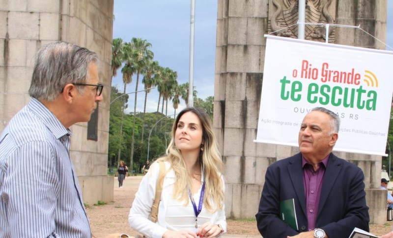 Na foto, aparecem da esquerda para a direita Mauro Renner, ouvidor do MPRS; Viviane Migliavacca, ouvidora-geral do Estado; e desembargador Altair de Lemos Jr., ouvidor-geral TJRS. Atrás deles, um banner com a marca do projeto O Rio Grande te Escuta, diante do Monumento ao Expedicionário, no parque da Redenção, na capital.