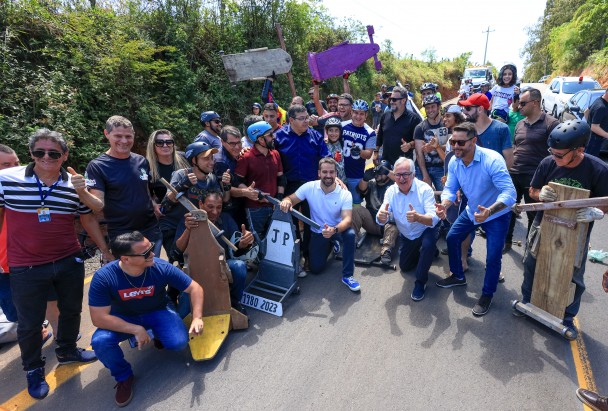 O governador Eduardo Leite aparece agachado no centro da imagem, junto de um grande grupo de pessoas com carrinhos de rolimã, que participaram de corrida organizada para celebrar a pavimentação de uma via em Sapucaia do Sul.