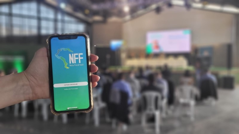 Imagem de uma mão segurando um celular que mostra a tela inicial do aplicativo Nota Fiscal Fácil.