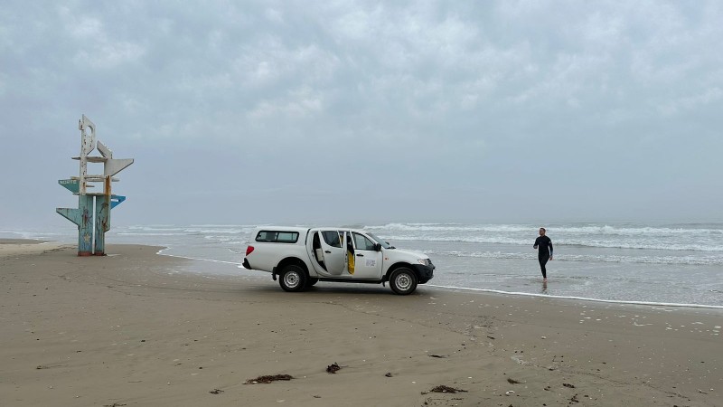 Imagem de um carro da Fepam em uma praia com uma pessoa saindo do mar com a coleta e água para análise do Projeto Balneabilidade 2023-2024.