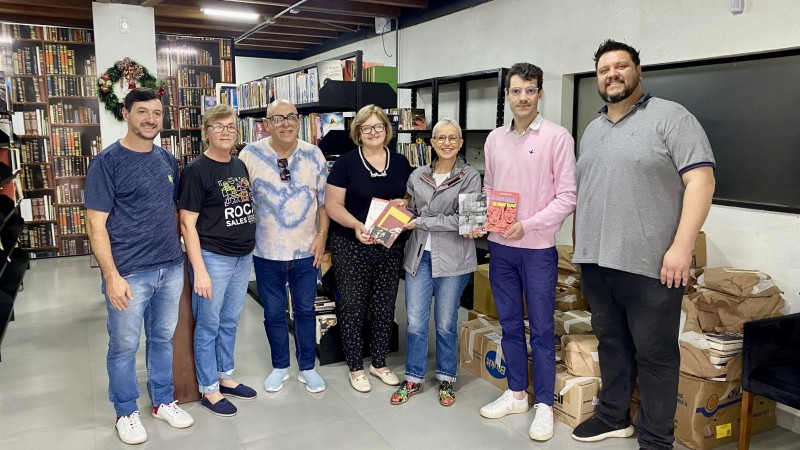 Foto posada dentro da biblioteca em Roca Sales na entrega dos livros. Quatro homens e três mulheres, entre elas a secretária da Cultura Beatriz Araújo. Alguns deles seguram livros nas mãos.