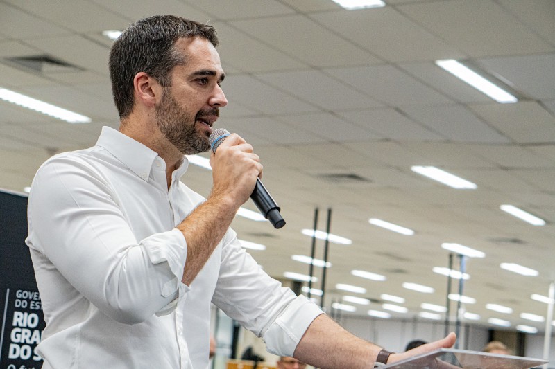 Foto em ambiente interno. Apenas o governador está na imagem. Ele está de pé, falando ao microfone.