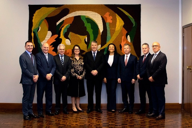 Foto posada da nova Diretoria do Banrisul que tomou posse em novembro de 2023. São sete homens e duas mulheres vestidos formalmente. Estão em um ambiente fechado e atrás deles há um enorme quadro na parede.