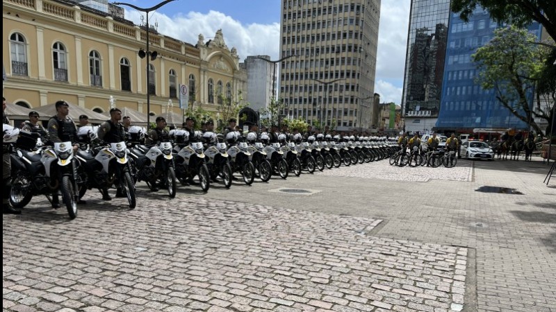Em frente ao Mercado Municipal de Porto Alegre, estão várias motos da Brigada Militar perfiladas. Ao lado de cada uma delas, há um policial militar.