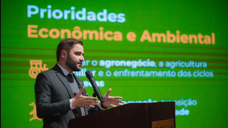 Gabriel atrás de um púlpito falando ao microfone para a plateia. Atrás dele há uma enorme tela onde se lê Prioridades Econômica e Ambiental.