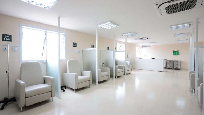Foto em ambiente fechado, plano geral. A imagem mostra uma sala de paredes, piso e móveis brancos. Ao fundo, à esquerda, há poltronas separadas por divisórias para tratamento.