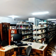 Foto interna mostra o Setor de Empréstimo da Biblioteca Pública Estadual, com diversas estantes cheias de livros, além de uma mesa com um computador em primeiro plano. 