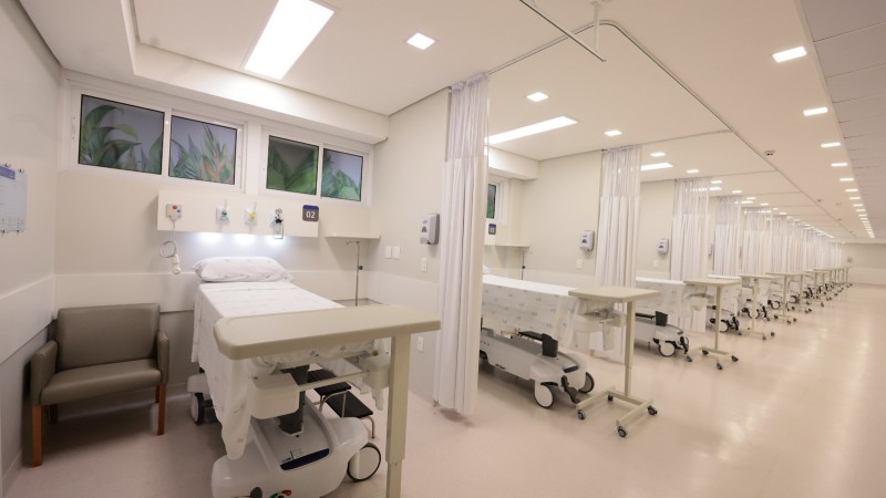 Foto no interior de uma ala hospitalar, de leitos. A imagem enquadra uma fileira de leitos vazios, do primeiro plano até o fundo no enquadramento.