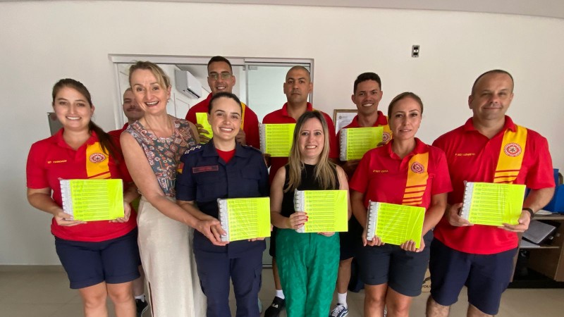 Foto posada com dez pessoas em pé e nove delas, possivelmente representantes dos bombeiros e das prefeituras, segurando cartelas das pulseira que foram distribuídas.