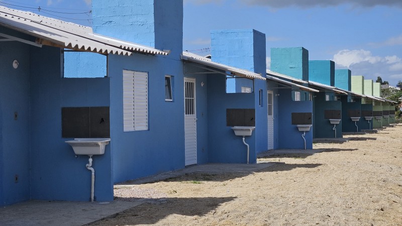 Foto em ambiente aberto de uma fileira de casas iguais de paredes azuis e tanques de louça branca.