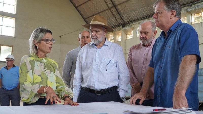 A secretária Izabel Matte mais à esquerda da imagem conversando com três homens, mais à direita. Eles estão em volta de uma mesa na qual parece estar o projeto relacionado às obras.