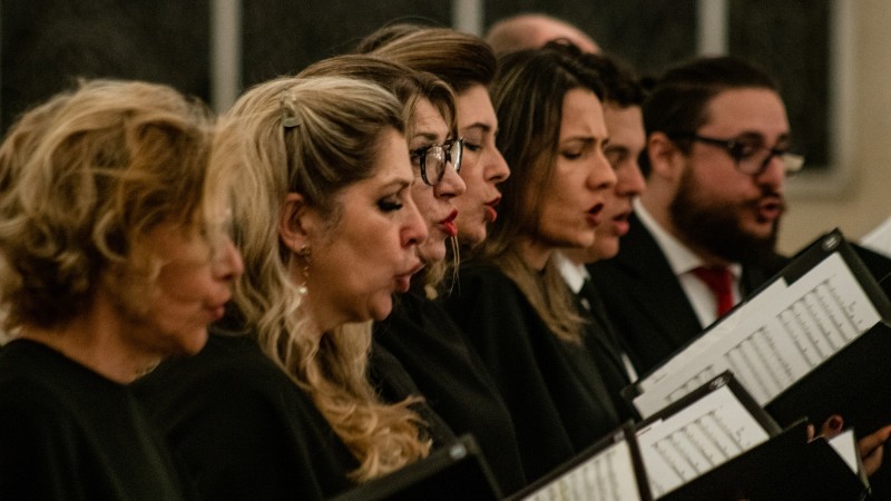Imagem do coro executando uma música. Da esquerda para a direita são cinco mulheres e três homens.