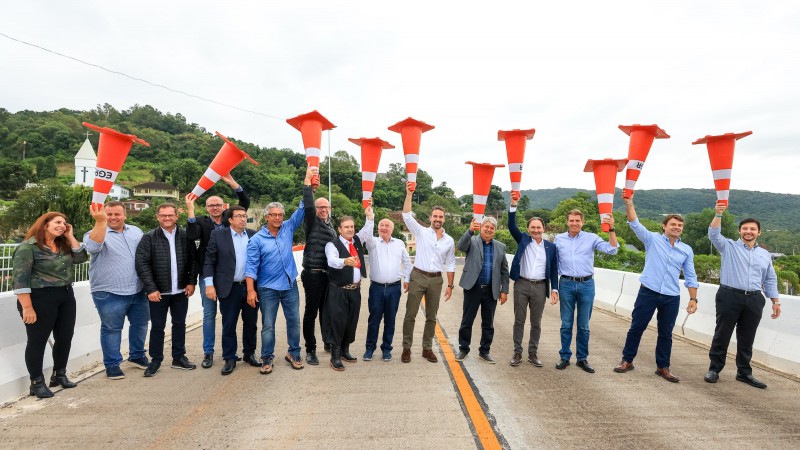 Foto posada em ambiente aberto, no viaduto. Cerca de 18 pessoas, com o governador ao meio, estão de pé sorrindo para a câmera. A maior parte deles está erguendo cones de sinalização, de cor laranja, para o alto.