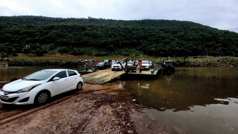 Imagem de carros desembarcando da balsa em uma das margens. Há um carro em destaque mais à esquerda e mais ao centro está a balsa com alguns carros.