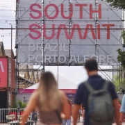 Foto da entrada do Cais Mauá na véspera de SSB 2024. Algumas pessoas de costas caminham e ao fundo vemos um enorme painel onde está escrito South Summit Brazil Porto Alegre.