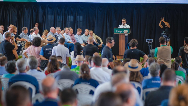 Gabriel falando atrás de um púlpito na abertura da Expoagro Afulbra 2024 para uma plateia que aparece de costas e de perfil na imagem.