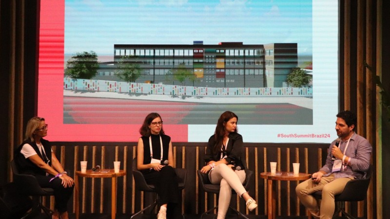 Três mulheres um homem sentados em cadeiras sobre um tablado apresentando o projeto desenvolvido em BIM para o Colégio Protasio Alves, em Porto Alegre. Ao fundo, um painel no qual está projetado o desenho da fachada da escola.